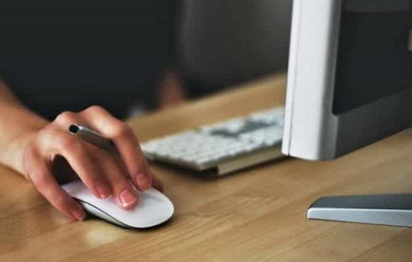 A person holding a computer mouse, working with a monitor and keyboard.