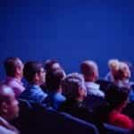 A crowd sits and watches in a theater space.