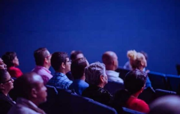 A crowd sits and watches in a theater space.