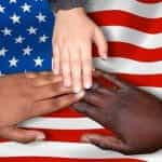Three hands joining together in unison over the flag of the United States.
