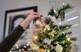A woman putting a bauble on a Christmas tree decorated with tinsel.