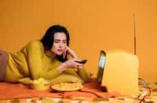 A woman in yellow watching a television, with snacks.