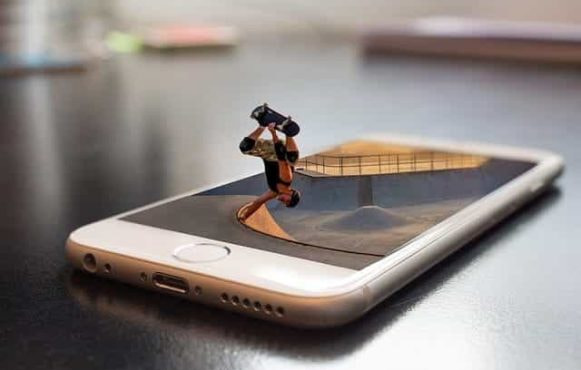 A skateboarder doing a trick while coming out of a smartphone screen.