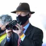Trainer Willie Mullins wearing a covid mask watching a horse race.