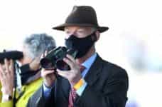Trainer Willie Mullins wearing a covid mask watching a horse race.
