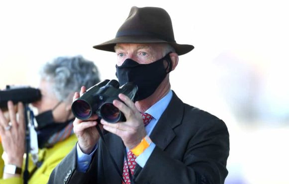 Trainer Willie Mullins wearing a covid mask watching a horse race.