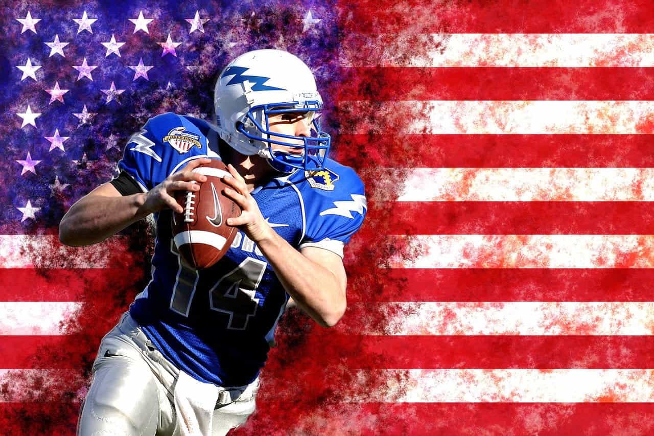 An American football player getting ready to throw the ball in front of the flag of the United States of America.