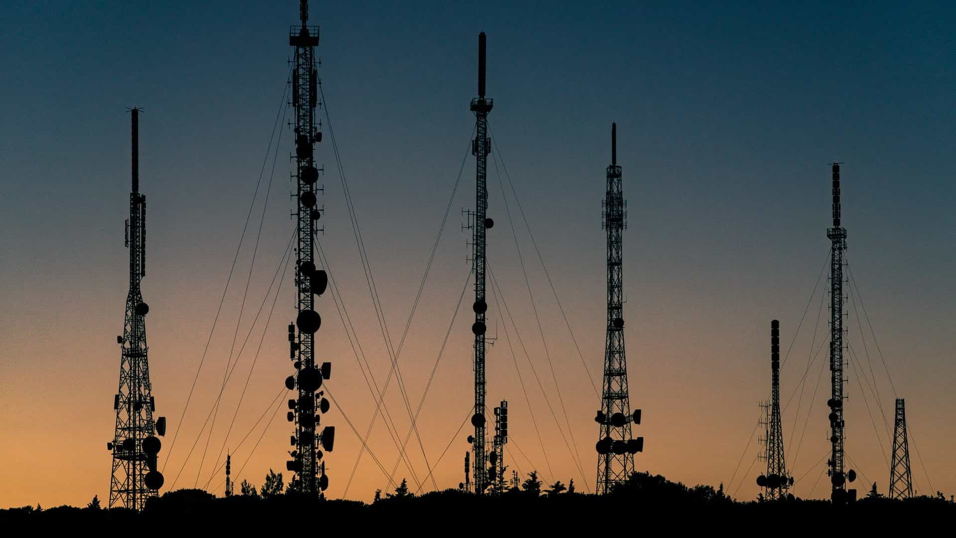Telecommunications towers stand silhouetted against a sunset.