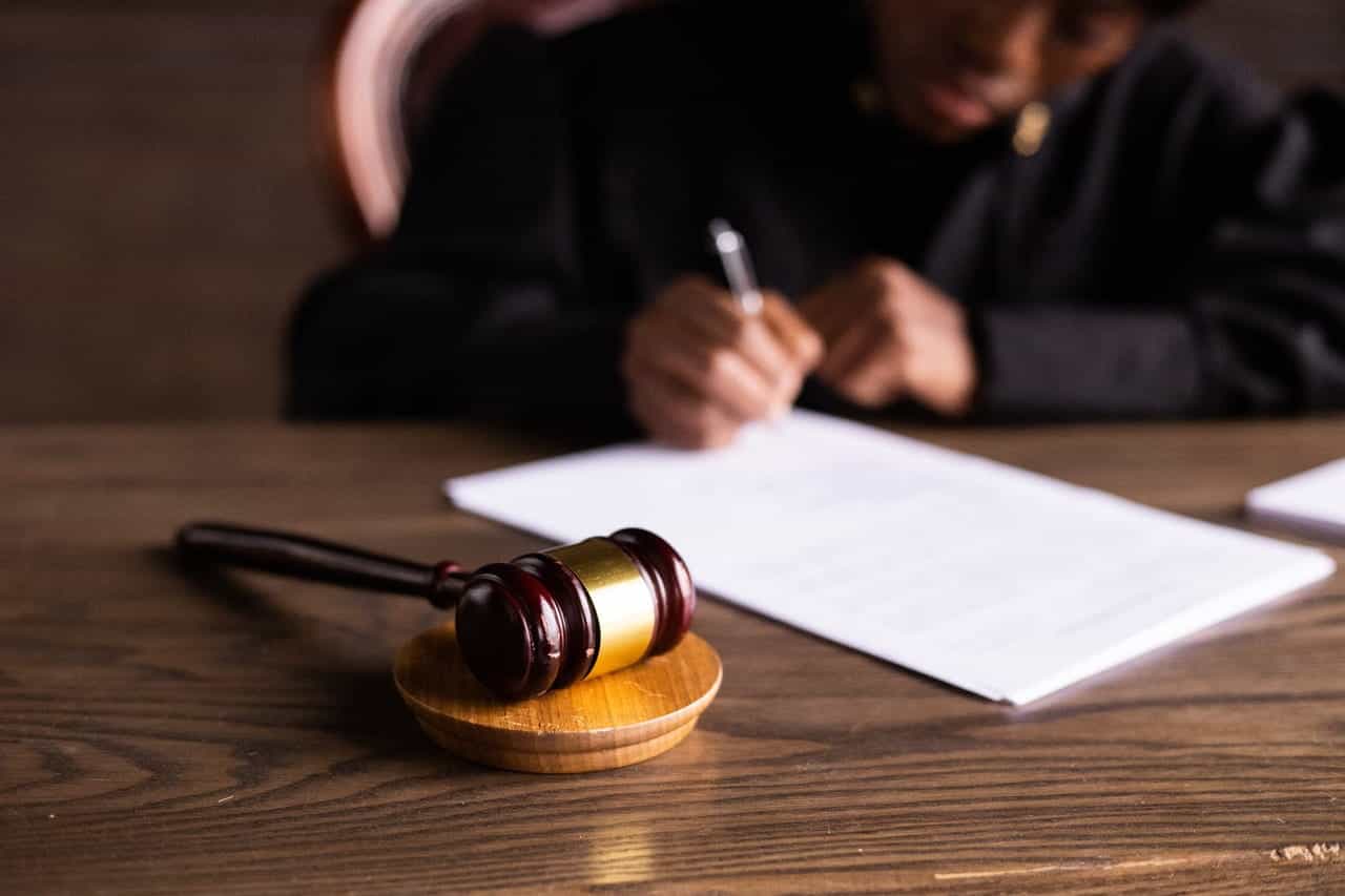 A judge writing a legal document next to a wooden gavel.