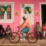 A man rides a bicycle in front of a pink building in Chile.