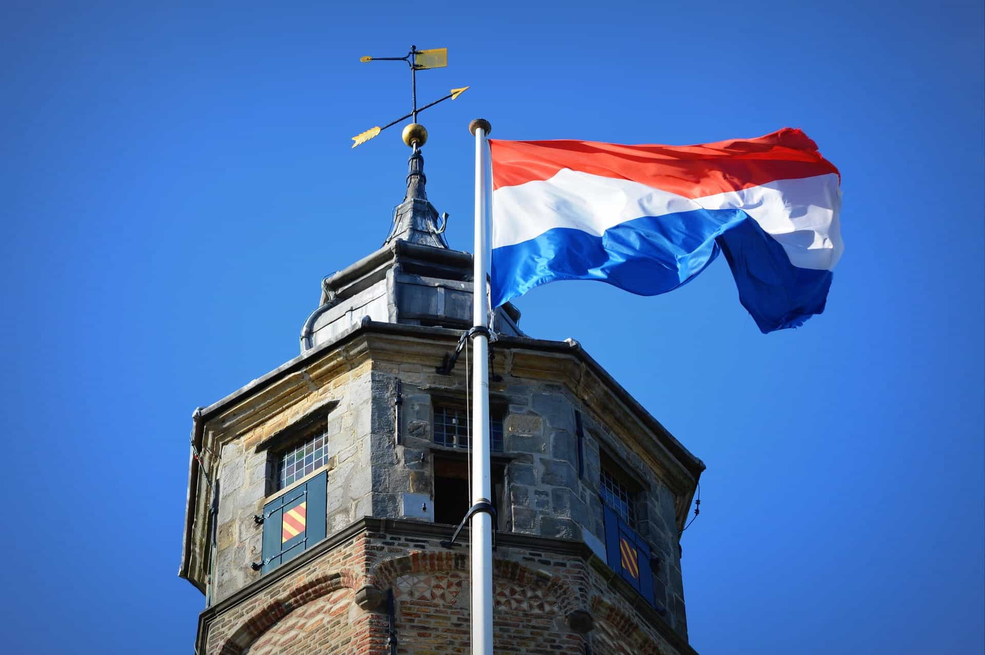 A Dutch flag on a flag pole flying in front of a tower