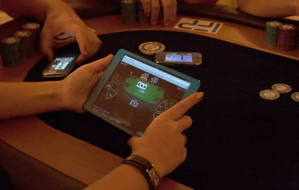 An individual plays online poker while sat at a traditional poker table.