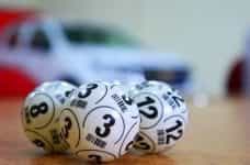 Three lottery balls resting on a table with a car in the background.