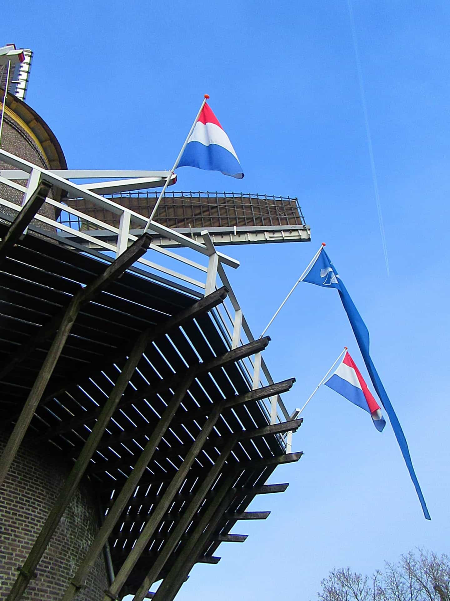 Top of a wooden mill with two Netherlands flags and one light blue flag