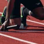A close up of the knees of a runner kneeling at the starting line on a race track.