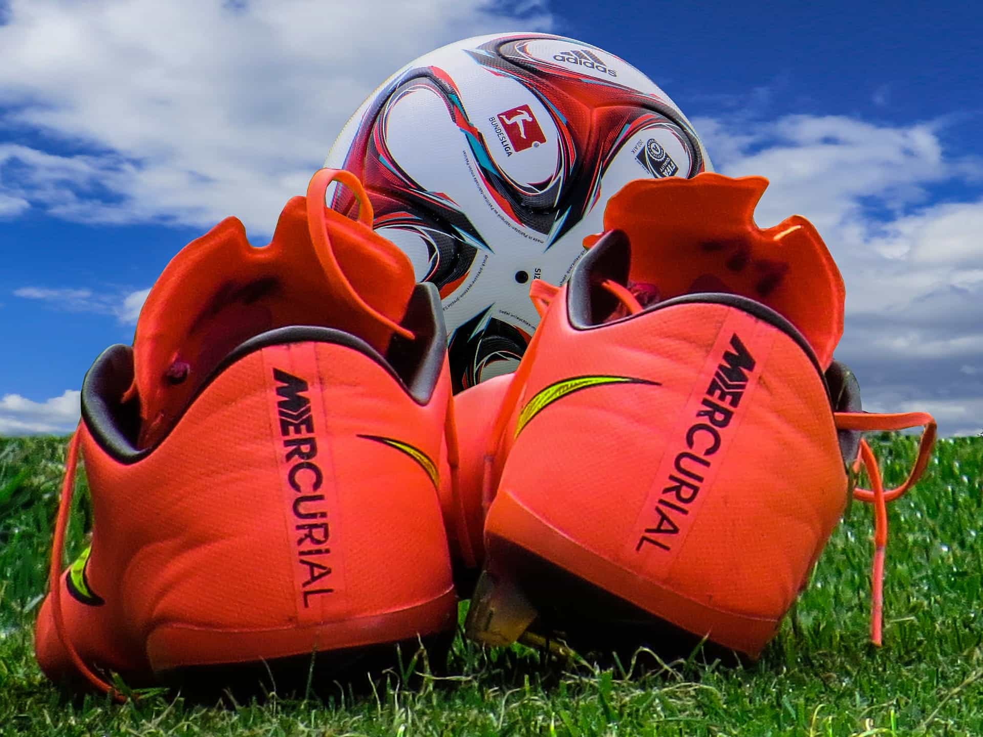 Orange football boots in the foreground with a football in the background
