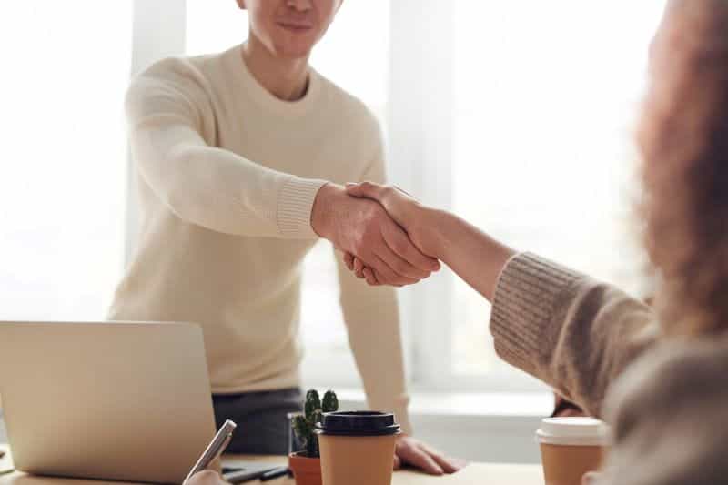 Two people shake hands across an office desk.