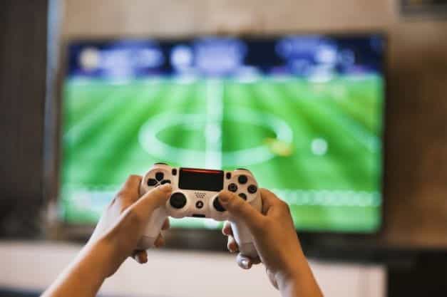 A video games controller is held up in front of a screen showing a football game.
