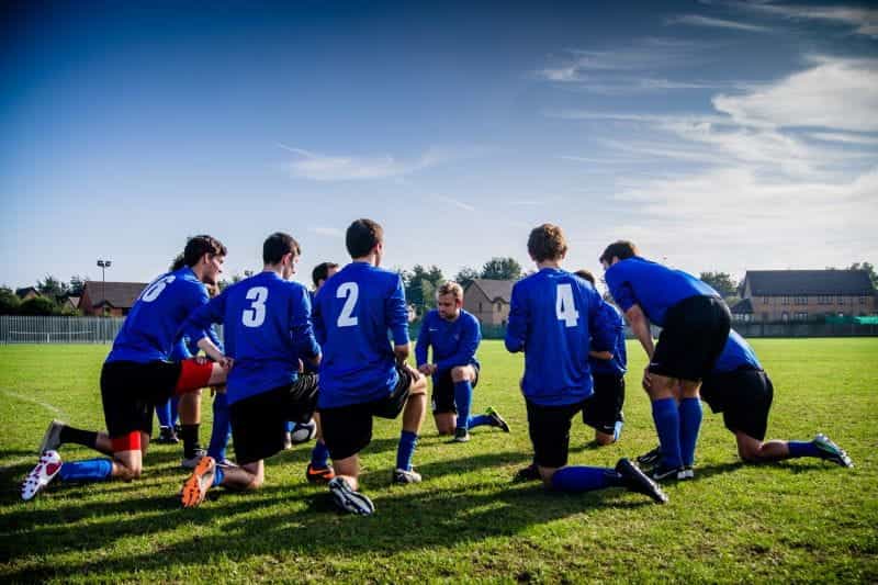 A team of football players kneeling on a grass pitch.