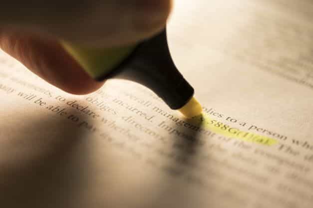 A yellow highlighter pen being used to highlight a passage in a written document.