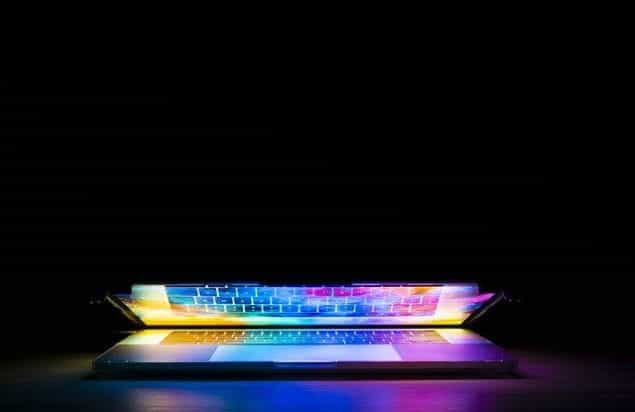 A laptop with its screen partially lifted up, revealing a bright multicolor image illuminating the laptop’s entire keyboard.