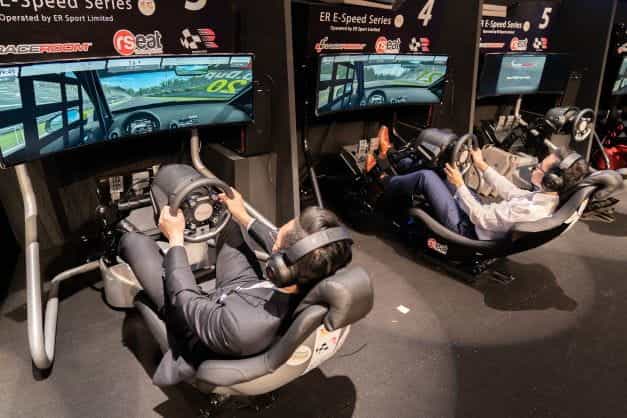 Two racing car simulators with drivers in arcade setting.