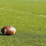 An American football resting on the grass of a football pitch.