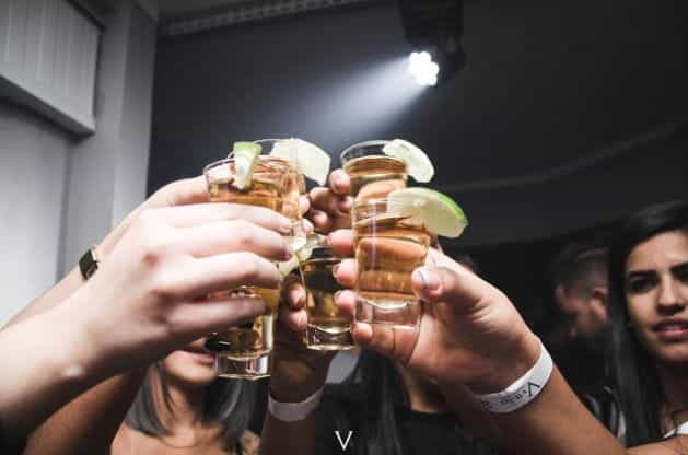 A group of people holding up shot glasses of alcohol in a bar.