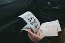 A hand holds several lottery tickets, while inside a car.