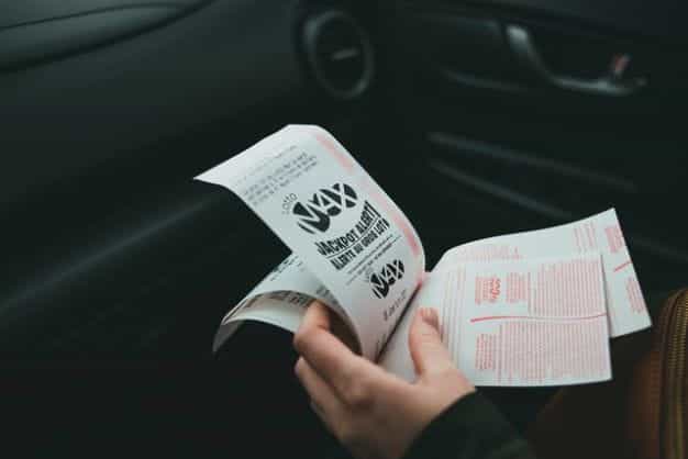 A hand holds several lottery tickets, while inside a car.