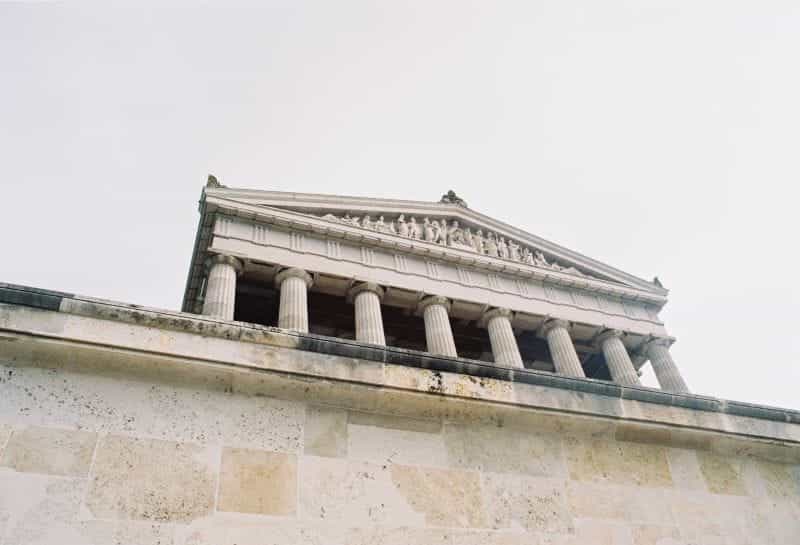 An old white court building with columns on its facade looms behind a wall.