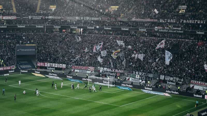 Football stadium with players by the goal and Frankfurt flags in the crowd.