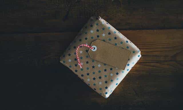 A small present in gift wrapping lying flat on a table, with a small tag on top of it.