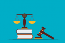 The scales of justice standing on two stacked books with a hammer and a gavel placed off to the side.