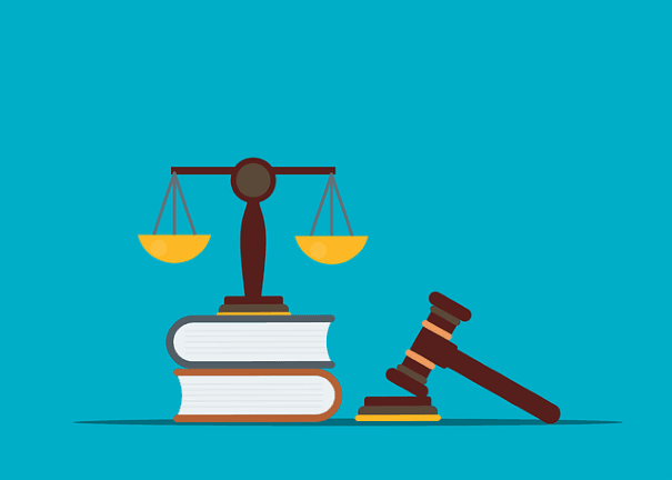 The scales of justice standing on two stacked books with a hammer and a gavel placed off to the side.