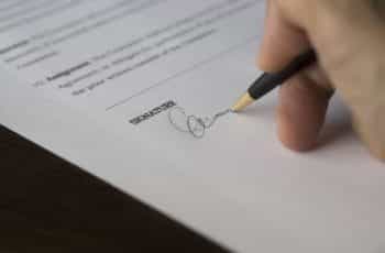 A hand signing a document with a pen.
