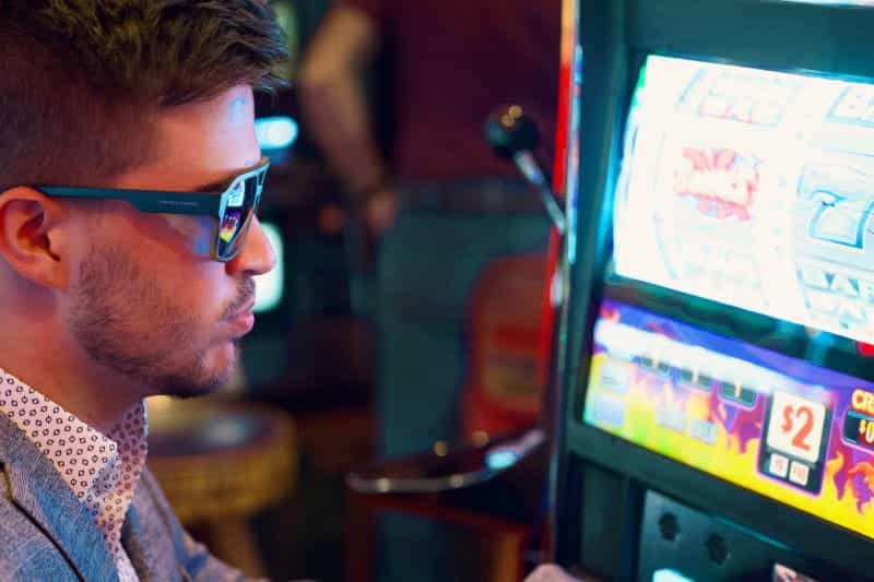 A man wearing sunglasses looks at a slot machine terminal screen.