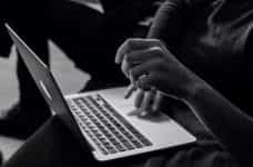 Someone uses a laptop on their lap, in black and white.