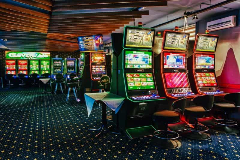 A room with green carpet and two rows of slot style gaming machines.