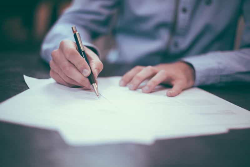 A person signs a document with a pen on top of a table.
