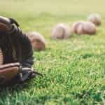 A brown leather baseball mitt with baseballs on grass.