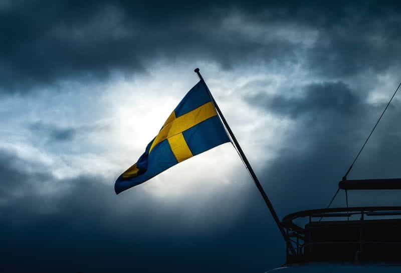 A Swedish flag, blue background offset yellow cross, flies against a stormy sky.