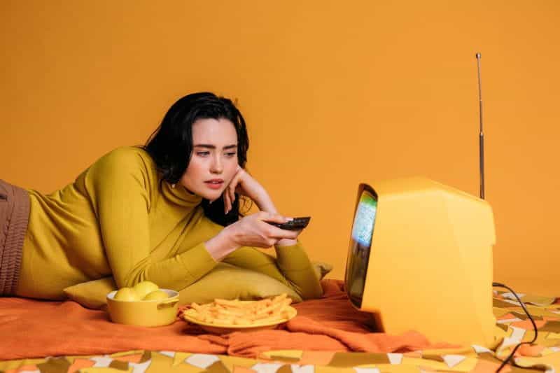 A woman watching television with bowls of snacks.