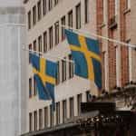 Two Swedish flags on poles on the front of a building.