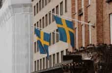 Two Swedish flags on poles on the front of a building.
