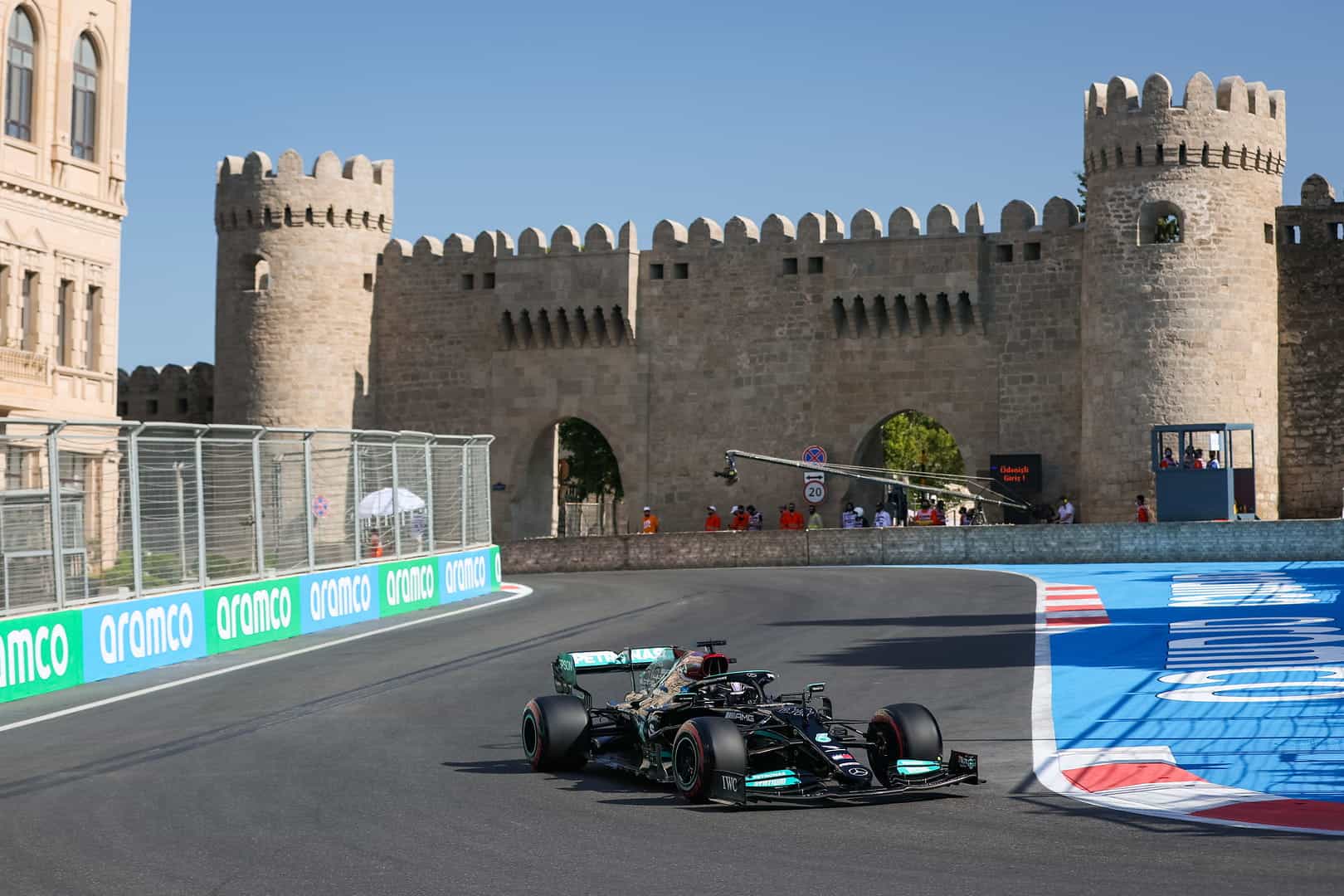 A Mercedes F1 car races around the Baku circuit with the historic city walls in the background.