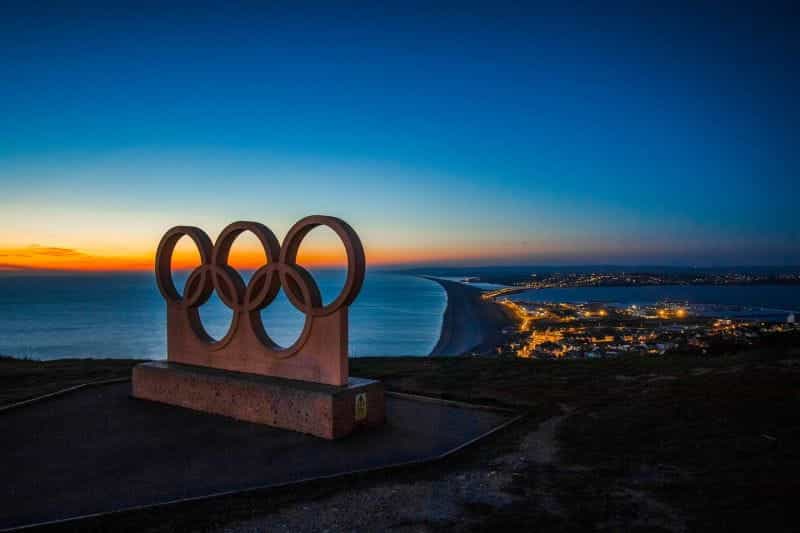 A statue of the Olympic rings above a city at night.