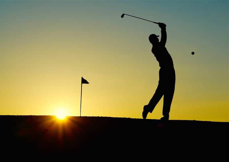 The silhouette of a golf player during sunset after swinging and hitting a golf ball on a golf course.
