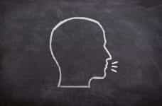 An outline of a speaking human head drawn in chalk on a chalkboard.