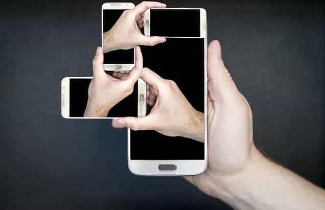 A hand holding out a smartphone, out of which several other hands also holding smartphones are emerging.
